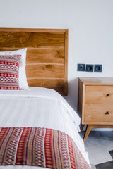 Bedroom interior, light wooden bedhead, wall, white bed sheets, red pillows. Minimal design