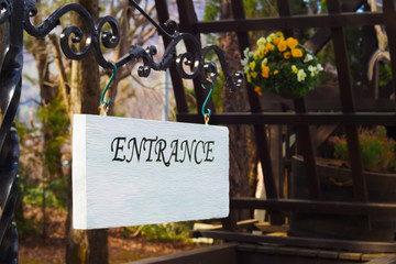 Entrance sign made of wood with white color hanging on a black steel beam.