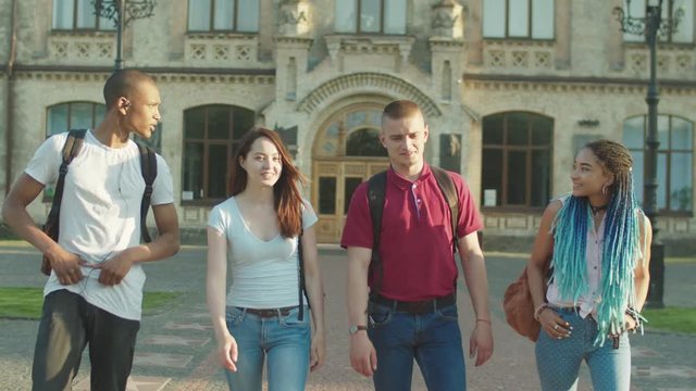 Positive diverse multi ethnic students leaving university and saying goodbye to each other in campus park. Multinational friends walking along park alley and hugging parting until next day of classes.