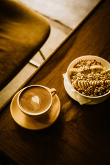 Cappuccino coffee with heart in yellow cup and plate from above. Warm toned filter effect.