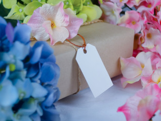 Brown gift box with blank paper labels and placed in the midst of blue and pink flowers