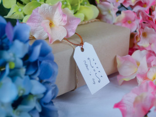 Brown gift box with greeting cards on Mother's Day  and placed in the midst of blue and pink flowers