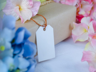 Brown gift box with blank paper labels and placed in the midst of blue and pink flowers
