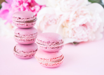 macaroons with strawberry and cocoa flavor lie on pink paper, against the background of delicate peony flowers