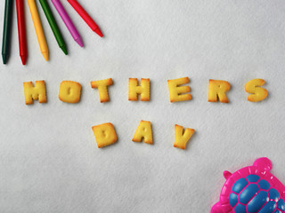 Biscuits, letters, shapes and colorful crayons,plastic toys arranged on a white background for Mother's Day
