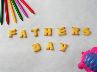 Biscuits, letters, shapes and colorful crayons,plastic toys arranged on a white background for Father's Day