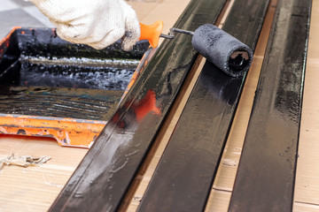 The painter wears cloth gloves, using a black paint roller on the steel rod.