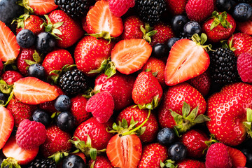 top view of fresh ripe strawberries, blueberries and blackberries on dark table with copy space