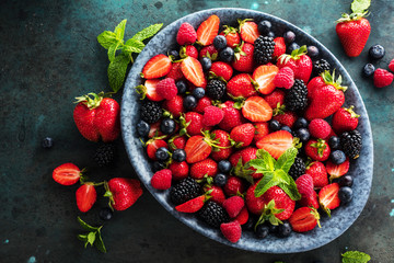 top view of fresh ripe strawberries, blueberries and blackberries on dark table with copy space