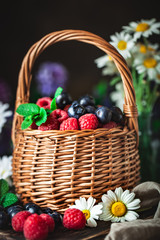 Fototapeta na wymiar Raspberries and blueberries in a basket with chamomile and leaves on a dark background. Summer and healthy food concept. Selective focus. Background with copy space.