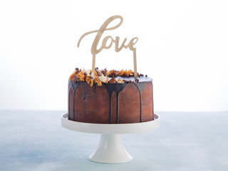 Wedding Cake with melting chocolate ganache and Love wood caketopper on a white background with space for text. Valentines day Celebration concept. Trendy Drip Cake.