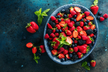 top view of fresh ripe strawberries, blueberries and blackberries on dark table with copy space