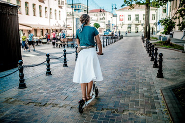 Obraz premium young woman on a white electric scooter in sunglasses walks around the city on a sunny day.