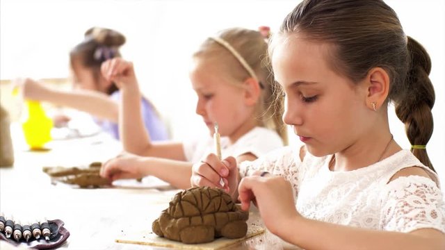 Master class in the manufacture of clay toys in art workshop. Children girls are sculpting turtles from clay using special tools in arts and crafts class.