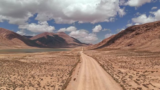 Aerial over gravel off road trail near arid desert mountains in sunny day.Pamir highway silk road trip adventure in Kyrgyzstan and Tajikistan desert,central Asia.4k drone flight establisher video