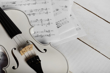 Close view of a violin and musical notes on white wooden table