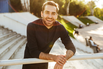 Handsome young strong sports happy man posing outdoors at the nature park location.