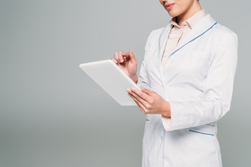 cropped shot of mixed race doctor in white coat using digital tablet isolated on grey