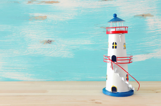 vacation and summer concept with vintage lighthouse over wooden table or shelf infront of pastel blue background