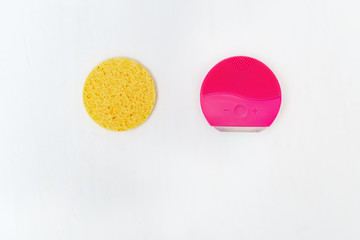 Silicone brush for face wash and traditional cosmetic sponge on white background with copy space. Skin cleansing. Facial care. Beauty blog concept. Flat lay. Top view.