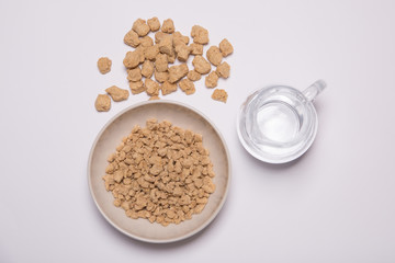 Proteína de soja texturizada fina y gruesa (carne vegana) sobre un fondo blanco y jarra de agua para rehidratarla. Sustituto de carne para vegetarianos y veganos.