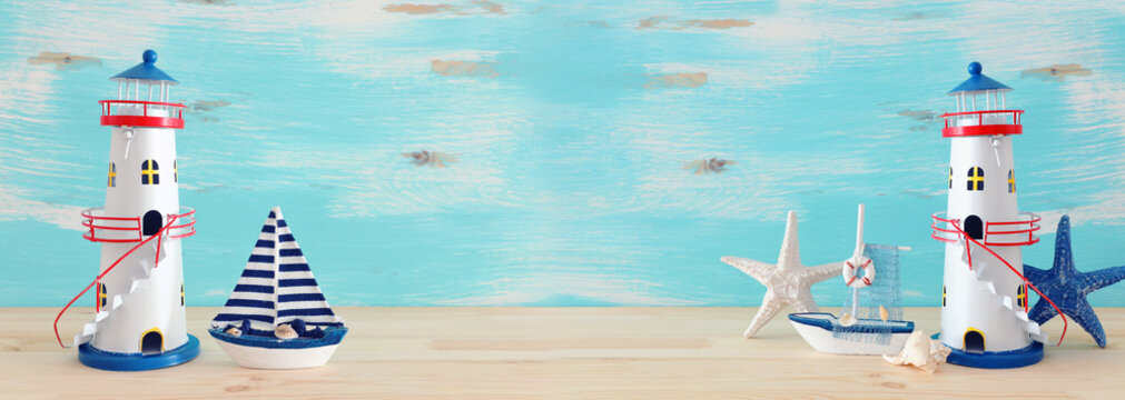 vacation and summer concept with vintage boat, starfish, lighthouse and seashells over wooden table or shelf infront of pastel blue background. banner