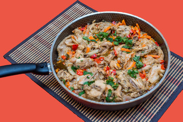 Pieces of rabbit stew with vegetables pepper, onion and herbs in a frying pan on the table. Appetizing delicious food for a festive dinner on a red background. Horizontal copy space, flatlay
