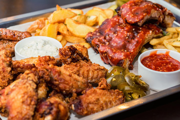 Dish of mixed meats. Grilled ribs, chicken wings and sausages with French fries