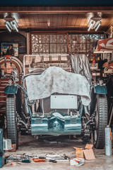 Retro vintage car covered by white cloth. Renovation project in the garage with lots of mechanical...