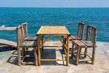 Bamboo table and wooden chairs in empty cafe next to sea water in tropical beach . Island Koh Phangan, Thailand