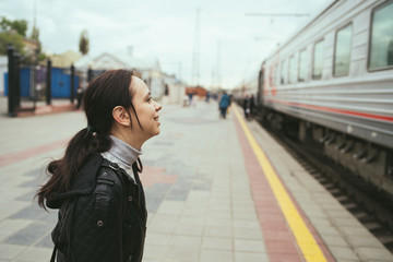 Obraz premium Young woman waiting for arrival of train. Side view unrecognizable young brunette female standing on platform and waiting for arrival of train
