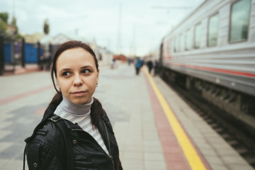 Obraz premium Young woman waiting for arrival of train. Side view unrecognizable young brunette female standing on platform and waiting for arrival of train