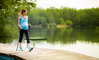 Fototapeta na wymiar Pregnant woman nordic walking outdoor, exercises during pregnancy