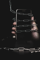 Smartphone with lock chain on a black background. Concept of social disease, social syndrome,...