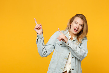 Portrait of amazed young woman in denim casual clothes keeping mouth open, pointing index fingers aside isolated on yellow orange background in studio. People lifestyle concept. Mock up copy space.