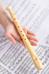 Plastic beige flute in the children's hand on the background of sheets with musical notes