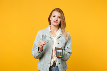 Fototapeta premium Attractive young woman holding wireless modern bank payment terminal to process and acquire credit card payments isolated on yellow orange background. People lifestyle concept. Mock up copy space.