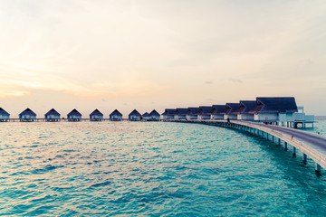Obraz premium Beautiful tropical sunset over Maldives island with water bungalow in hotel resort