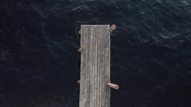 Aerial, top down, drone shot, rising, above the end of a wooden pier, at Vuoniemi cape, surrounded by calm waters of lake Saimaa, on a sunny, spring evening, in North Karelia, Finland