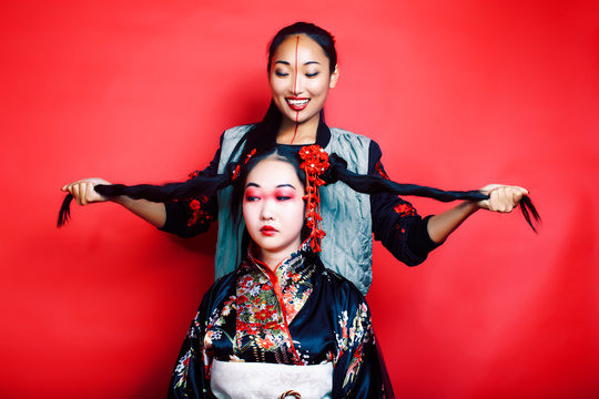 Two Pretty Geisha Girls Friends: Modern Asian Woman And Traditional Wearing Kimono Posing Cheerful On Red Background 