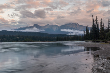 A riverside view at sunset of the Athabasca River as it weaves its way through the Jasper National Park, Canada, on a cloudy day, low clouds hugging the landscape