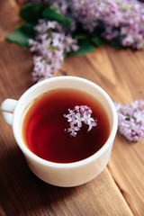 branches of blooming lilacs and a cup of tea on a wooden background