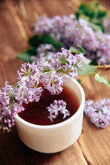 Fototapeta na wymiar branches of blooming lilacs and a cup of tea on a wooden background