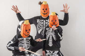 Happy friendly family of musicians in carnival costumes, boys and young mother play drum and try to...