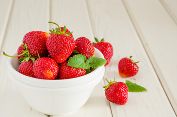 Fresh ripe strawberries in a bowl on a white wooden background.