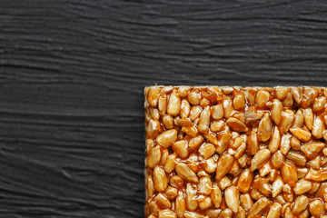Tile kozinaki from sunflower seeds on a black textural background. Delicious oriental sweets Gozinaki from sunflower seeds, sesame seeds and peanuts, covered with honey with a shiny icing
