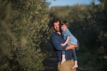 Father with small daughter standing outdoors by olive tree.