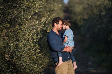 Father with small daughter standing outdoors by olive tree.