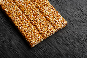 Tile kozinaki from sunflower seeds on a black textural background. Delicious oriental sweets Gozinaki from sunflower seeds, sesame seeds and peanuts, covered with honey with a shiny icing