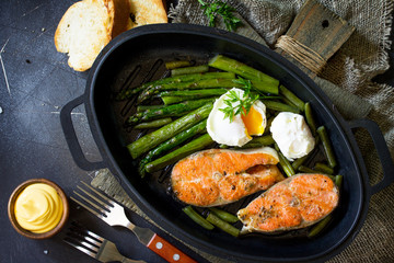 Salmon fish steak grilled with asparagus, poached egg in a frying pan on a rustic stone table. Healthy food. Top view flat lay.  Free space for your text.